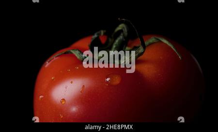 Gouttes d'eau recouvertes de tomates mûres rouges isolées sur du noir.Cadre.Tomate isolée sur fond noir brillant avec réflexion réaliste et gouttes d'eau. Banque D'Images