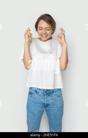 Une femme caucasienne faisant un geste avec le doigt a traversé le sourire avec espoir et les yeux fermés.Visage de beauté.Isolé sur fond blanc.Prise de vue en studio. Banque D'Images