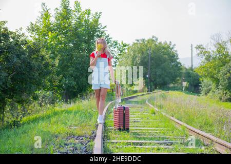 une fille avec un chapeau marche sur les rails avec une valise Banque D'Images