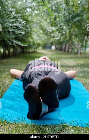 Une femme se trouve sur un tapis de sport sur une pelouse verte.Fin de l'entraînement physique.Entraînement en plein air. Banque D'Images