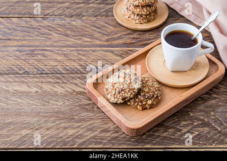 Des biscuits diététiques à base de flocons d'avoine avec des graines de sésame et de lin sont servis pour le petit-déjeuner sur un plateau en bois avec du café fraîchement moulu Banque D'Images