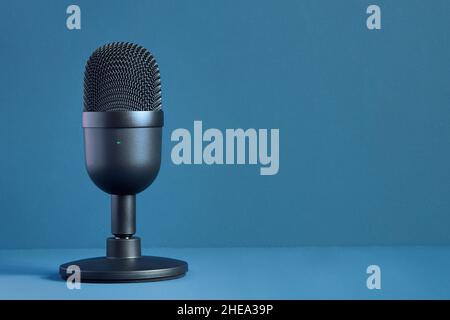 Image minimaliste d'un microphone noir moderne et élégant pour la diffusion et les jeux sur un fond bleu coloré avec texture et espace de copie.T Banque D'Images