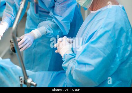 Concentrez-vous de manière sélective sur les mains du chirurgien portant des gants en latex blanc dans la salle d'opération.Un médecin en uniforme dans la salle d'opération se tient avec ses doigts clastés dans des gants stériles. Banque D'Images