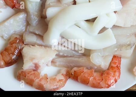 Gros plan sur des rondelles de calmar fraîches sur du merlu, du lotte et des crevettes fraîches sur une assiette blanche. Banque D'Images