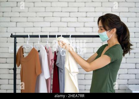 Un jeune ouvrier de blanchisserie asiatique portant un masque facial en regardant le tissu avant du suspendre.Atmosphère de travail dans la buanderie.Concept de nouvelle normale Banque D'Images