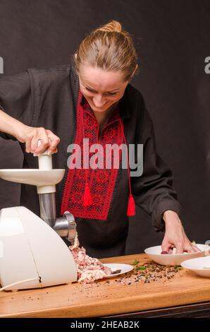 Femme utilisant un moulin pour la préparation de viande hachée dans la cuisine. Banque D'Images