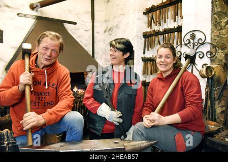 16 décembre 2021, Saxe, Leipzig: Rire, le forgeron d'art Andreas Althammer se tient devant le feu de forge à l'enclume avec ses filles, le maître métallurgiste et chef actuel de la forge, Elisabeth Althammer-Kluge (M) et le forgeron de métal et compagnon Claudia Süßmeyer.Althammer, qui a fondé sa forge artistique il y a 45 ans, est très heureux que ses deux filles aient repris les affaires de l'artisan et qu'il lui-même, avec ses nombreuses années d'expérience, puisse être à portée de main comme conseiller.(À dpa KORR: 'L'artisanat reste dans la famille - les filles prennent le contrôle de la forge d'art') Ph Banque D'Images