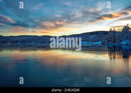 Le Vollsfjord recouvert de glace et le ciel coloré se reflète dans la glace.Paysage d'hiver avec îles, huttes, mer, rochers enneigés, ciel bleu,réflexion au coucher du soleil., Banque D'Images