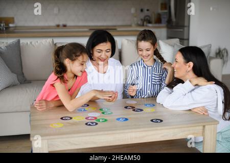 Petites filles heureuses avec mère et grand-mère jouant des cartes à l'intérieur à la maison. Banque D'Images