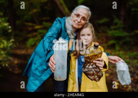 Petite fille avec grand-mère montrant les déchets de plastique ce qu'ils ont trouvé des outoors en forêt. Banque D'Images