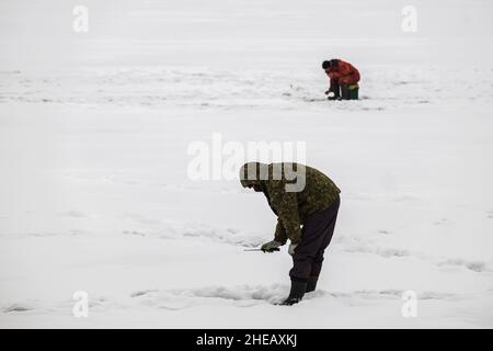 Pêche sous la glace.Pêche d'hiver sur la glace du lac (réservoir) par temps froid. Pêcheurs aux costumes chaleureux Banque D'Images