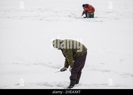 Pêche sous la glace.Pêche d'hiver sur la glace du lac (réservoir) par temps froid. Pêcheurs aux costumes chaleureux Banque D'Images