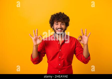 Je vais bien.Portrait d'un homme joyeux aux cheveux bruns avec barbe et moustache dans une chemise décontractée, regardant l'appareil photo et montrant un geste de main correct.Studio d'intérieur isolé sur fond orange Banque D'Images