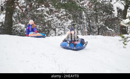 Les enfants adorables se traînaient et s'amusaient dans la neige.Un petit enfant glisse rapidement sur un traîneau.Crier avec joie.C'est une journée d'hiver très lumineuse. Banque D'Images