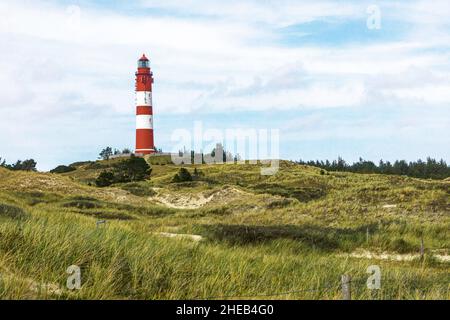 Grand bâtiment de phare rayé rouge et blanc sur une petite colline. Paysage côtier sablonneux avec végétation verte et sentiers. Jour d'été en mer Banque D'Images