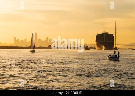 Les yachts et les bateaux à conteneurs géants se dirigent vers le port d'Oakland tandis que le soleil se couche sur la silhouette de San Francisco.Californie, États-Unis Banque D'Images