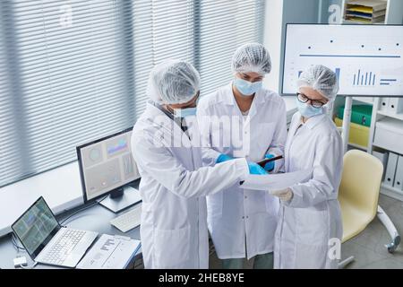 Groupe de médecins en manteaux blancs masques et gants discutant de documents médicaux ensemble tout en étant debout au bureau Banque D'Images