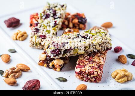 Barres de granola d'énergie avec différentes graines, noix et fruits secs et baies sur un fond de marbre blanc.Concept d'en-cas sain. Banque D'Images