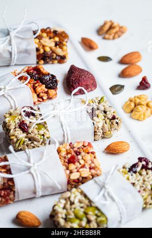 Barres de granola d'énergie avec différentes graines, noix et fruits secs et baies sur un fond de marbre blanc.Concept d'en-cas sain. Banque D'Images