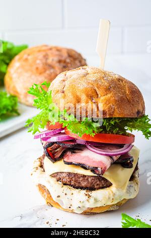 Cheeseburger maison avec bacon, légumes et sauce, fond blanc.Concept de restauration rapide maison. Banque D'Images