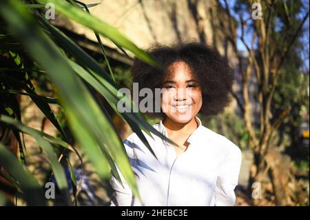 Mode gros plan portrait élégant de jeune beauté naturelle attrayante femme afro-américaine avec cheveux afro en chemise blanche posant à l'extérieur avec paume verte.Bonne dame rire avec un sourire et des dents parfaits Banque D'Images