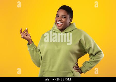 Bonne dame afro-américaine surdimensionnée qui se croque les doigts sur fond jaune Banque D'Images