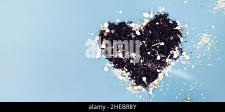 Coeur fait de feuilles de thé noir avec jasmin sur fond bleu.Coeur sous forme de thé Banque D'Images