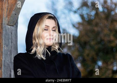 belle femme blonde vêtue de noir avec les yeux fermés pensant sourire Banque D'Images