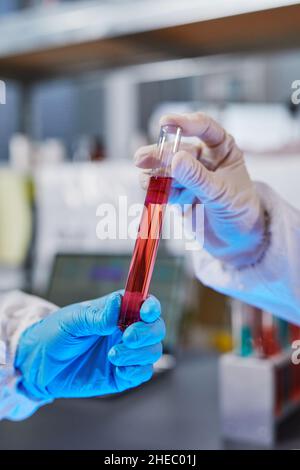 Gros plan du chercheur en gants de protection tenant le tube à essai avec du liquide rouge pendant l'expérience scientifique Banque D'Images