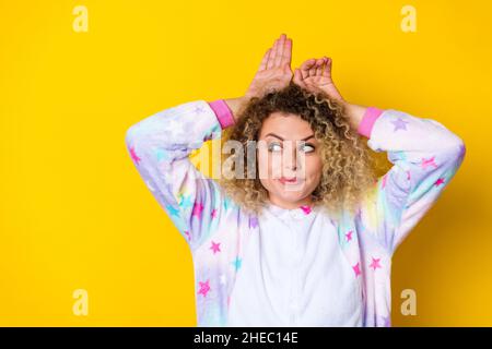 Portrait d'une jolie fille à poil ondulé et à poil ondulé dans un pyjama montrant des oreilles qui se bertent isolées sur un fond jaune vif Banque D'Images