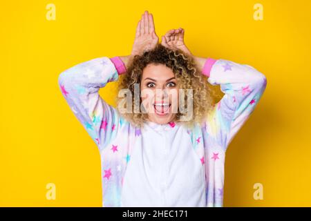 Portrait d'une petite fille à poil ondulé dans un pyjama avec des oreilles amusantes isolées sur un fond jaune éclatant Banque D'Images