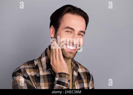 Portrait d'un joli homme gai bien entretenu portant une chemise à carreaux touchant le visage barbe isolée sur fond gris Banque D'Images