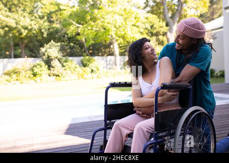 Homme afro-américain embrassant sa femme handicapée en fauteuil roulant et souriant à l'extérieur Banque D'Images