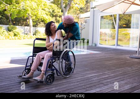 Homme afro-américain embrassant sa femme handicapée en fauteuil roulant et souriant à l'extérieur Banque D'Images