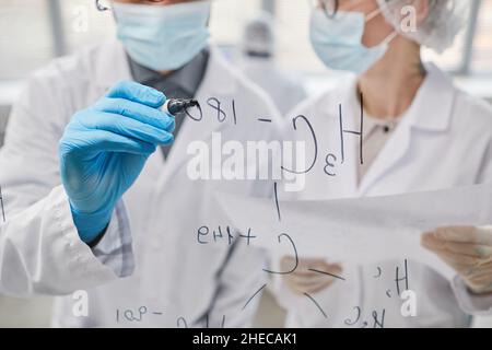 Gros plan de deux scientifiques qui écrivent des formules chimiques sur des planches de verre et en discutent en équipe Banque D'Images