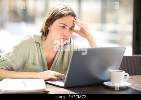 Un étudiant frustré vérifie le contenu en ligne sur un ordinateur portable dans un café Banque D'Images