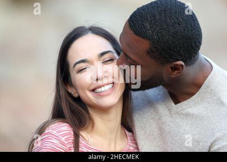 Homme heureux avec la peau noire embrassant sur la joue une femme de beauté à l'extérieur Banque D'Images