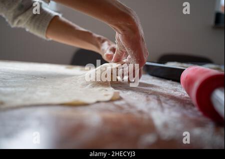 Vue à angle bas d'une femme tirant et étirant la pâte vegan maison roulé sur une table à manger maison. Banque D'Images