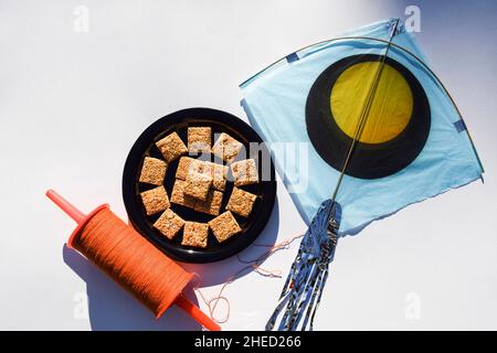 Rajgira chikki ou graines d'Amaranth avec barre de bonbons de jaggery faite pendant le festival de Makarsankranti.Arrière-plan d'un grand cerf-volant rose avec un espace de copie de bobine orange Banque D'Images