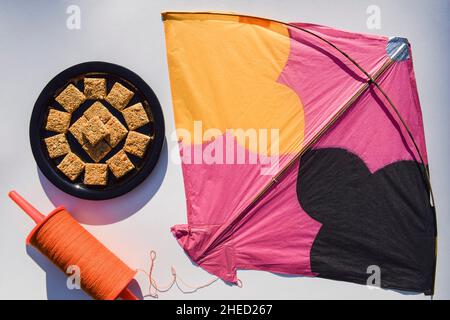 Rajgira chikki ou graines d'Amaranth avec barre de bonbons de jaggery faite pendant le festival de Makarsankranti.Arrière-plan d'un grand cerf-volant rose avec un espace de copie de bobine orange Banque D'Images