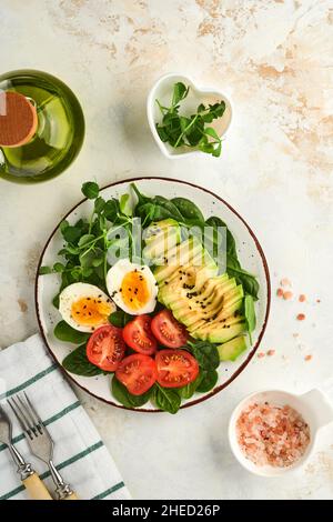 Avocat, tomates cerises, œufs d'épinards et de poulet, petits pois et graines de sésame noir salade fraîche dans un bol sur fond de table en pierre blanche. En bonne santé Banque D'Images