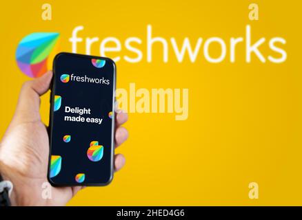 San Francisco, USA, décembre 2021: Main tenant un téléphone avec l'application mobile Freshworks sur l'écran.Freshworks logo flou sur un backgrou jaune Banque D'Images