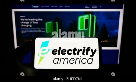 Personne tenant un téléphone mobile avec le logo de l'entreprise américaine de charge de VE électrify America LLC sur l'écran devant la page Web.Mise au point sur l'affichage du téléphone. Banque D'Images