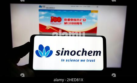 Personne tenant un smartphone avec le logo de la société chinoise de produits chimiques Sinochem Corporation sur l'écran devant le site Web.Mise au point sur l'affichage du téléphone. Banque D'Images