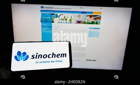 Personne tenant un téléphone portable avec le logo de la société chinoise de produits chimiques Sinochem Corporation à l'écran en face de la page Web.Mise au point sur l'affichage du téléphone. Banque D'Images