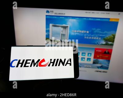 Personne tenant un smartphone avec le logo de China National Chemical Corporation (ChemChina) sur l'écran devant le site Web.Mise au point sur l'affichage du téléphone. Banque D'Images