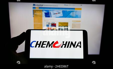 Personne tenant un téléphone portable avec le logo de la China National Chemical Corporation (ChemChina) à l'écran en face de la page Web.Mise au point sur l'affichage du téléphone. Banque D'Images