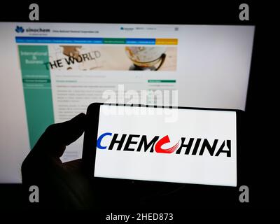 Personne tenant un téléphone portable avec le logo de la China National Chemical Corporation (ChemChina) à l'écran devant la page Web.Mise au point sur l'affichage du téléphone. Banque D'Images