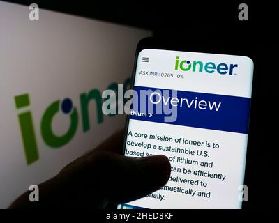 Personne tenant un téléphone portable avec la page Web de la compagnie minière australienne ioneer Ltd. À l'écran avec le logo.Concentrez-vous sur le centre de l'écran du téléphone. Banque D'Images