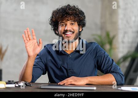 Portrait d'un homme indépendant, souriant et amical, utilisant un ordinateur portable et regardant la caméra.Un homme mauricien latin indien dans une chemise élégante et décontractée qui agite, tout en travaillant à distance Banque D'Images